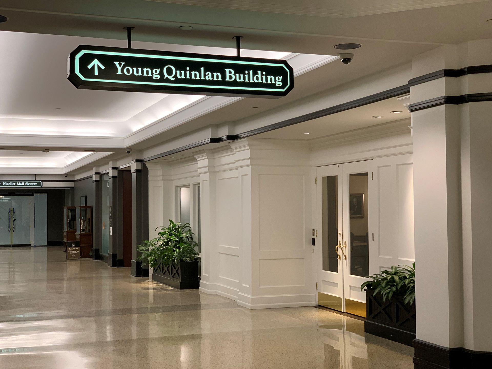 Sign pointing to Young Quinlan Building; skyway with white walls, columns, and doors.