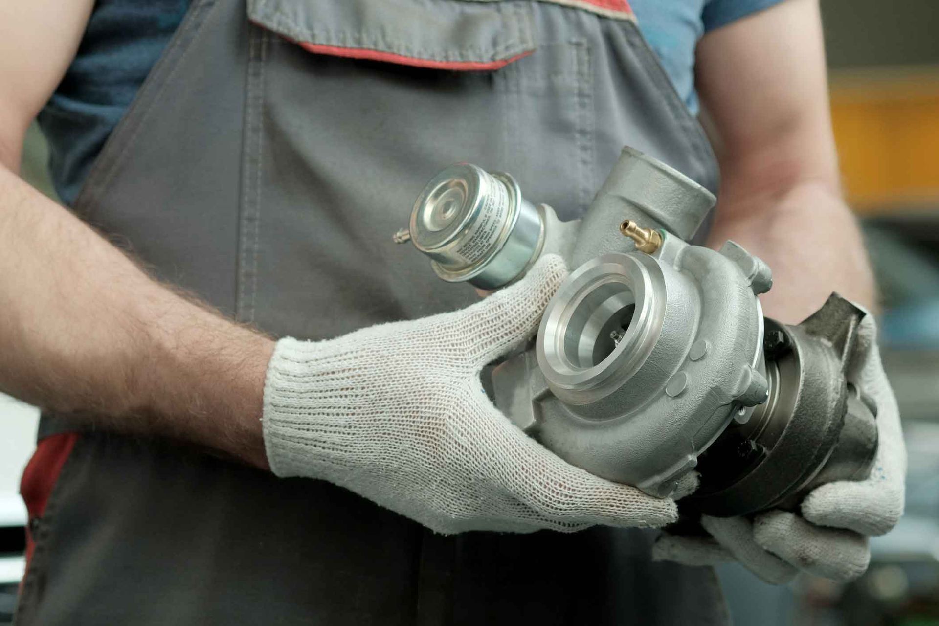 A man wearing gloves is holding a turbocharger in his hands.