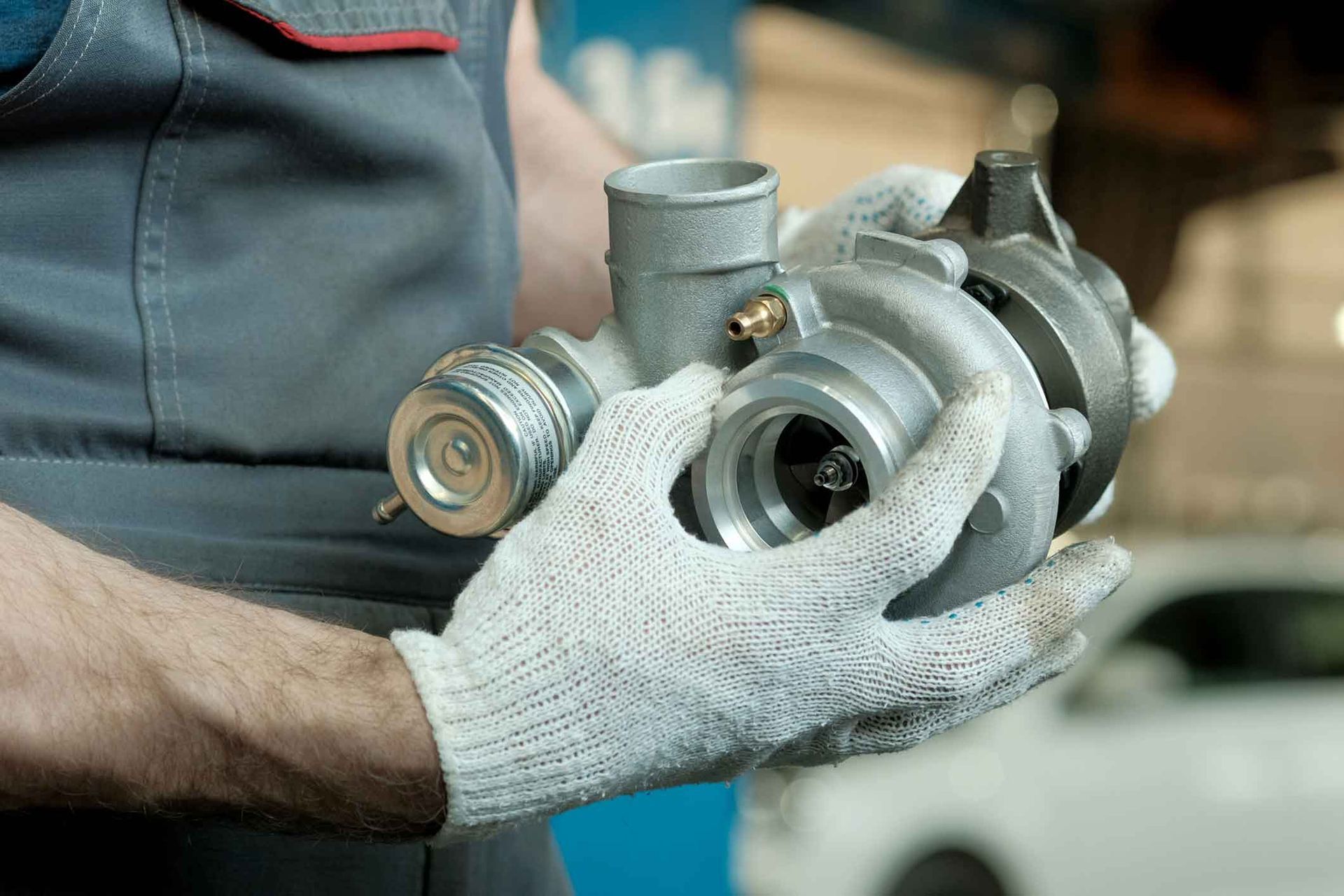 A man wearing gloves is holding a turbocharger in his hands.
