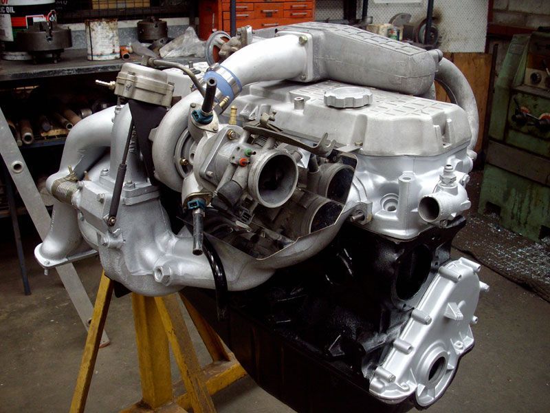 A car engine is sitting on a yellow stand in a garage