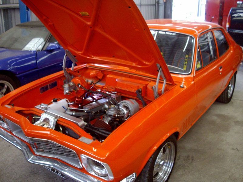 An orange car with the hood up in a garage