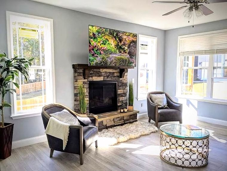 A living room with a fireplace , chairs , a coffee table and a ceiling fan.