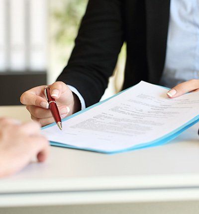 Persona con traje de negocios apuntando con bolígrafo a un documento para firmar.