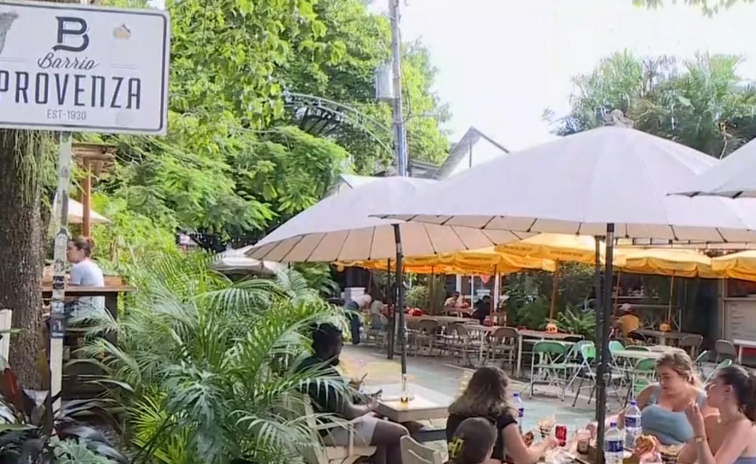 A group of people are sitting at tables under umbrellas in front of a sign that says provenza