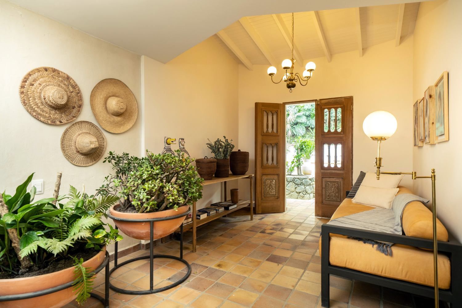 A living room with a couch , potted plants , and straw hats on the wall.