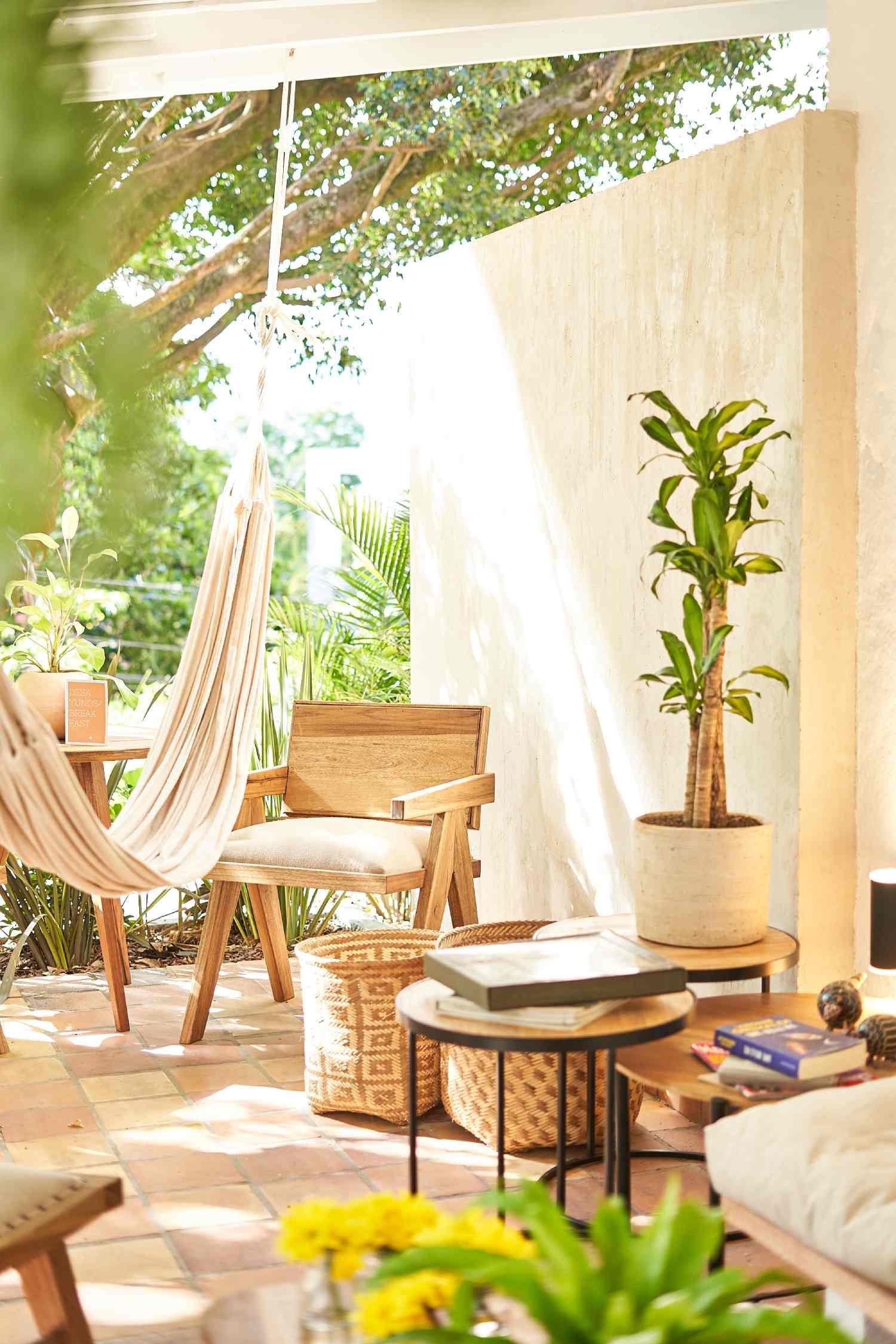 A living room with a hammock , chairs , tables and a potted plant.