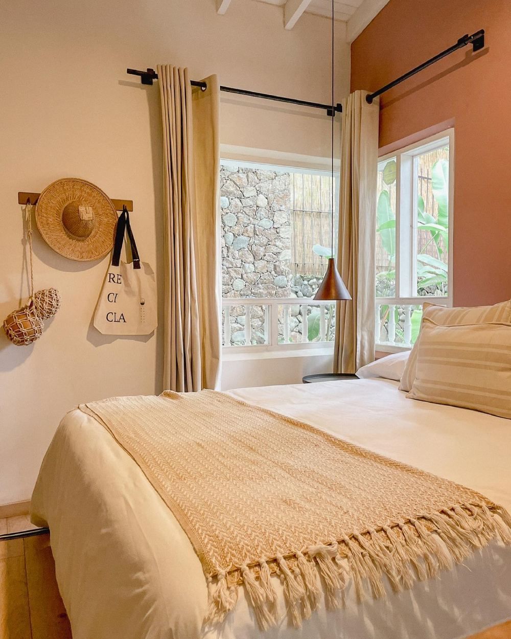 A bedroom with a bed , a window and a straw hat hanging on the wall.