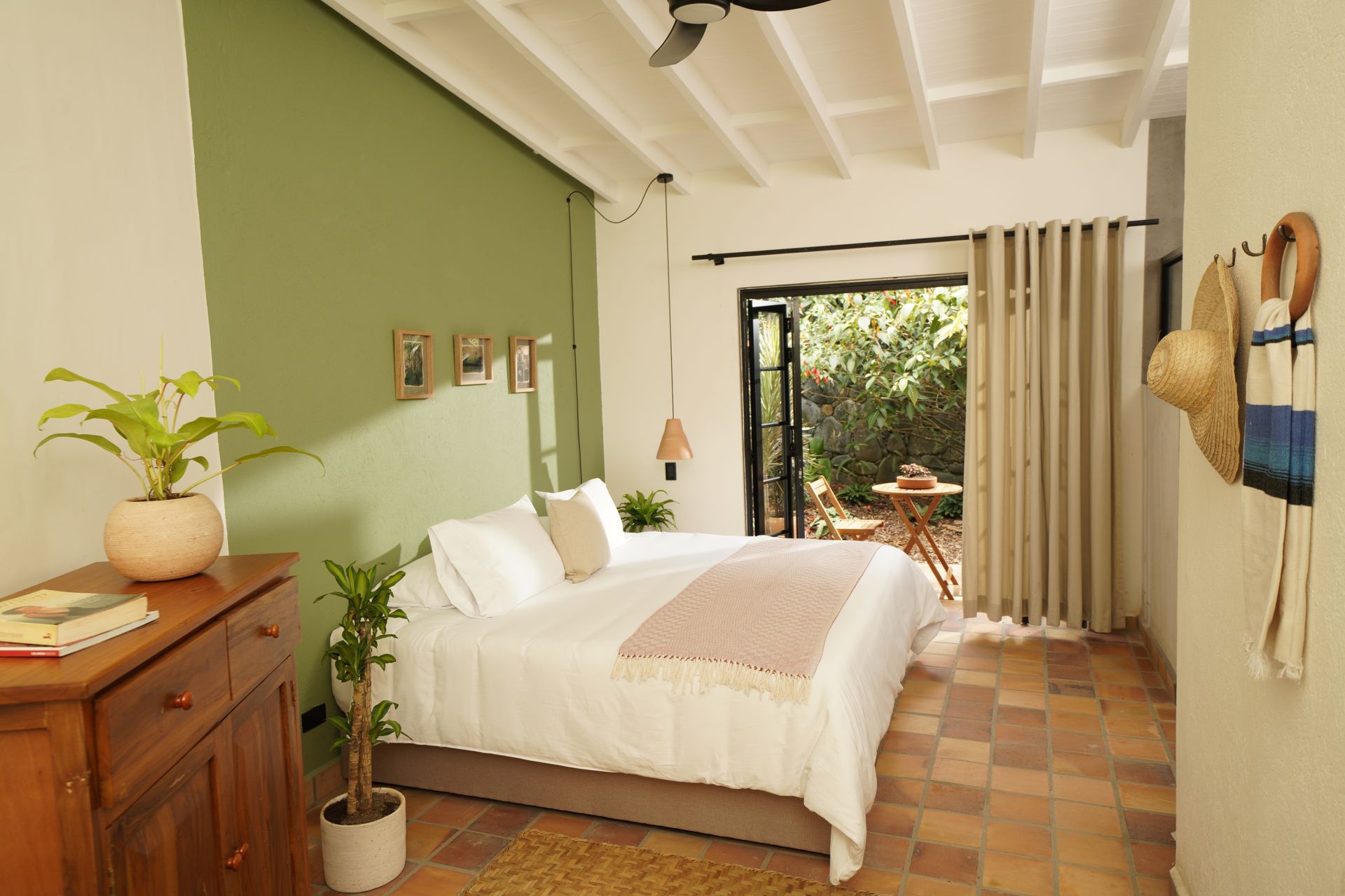 Bedroom with bed, open door to patio, wooden dresser, green wall, and potted plants.