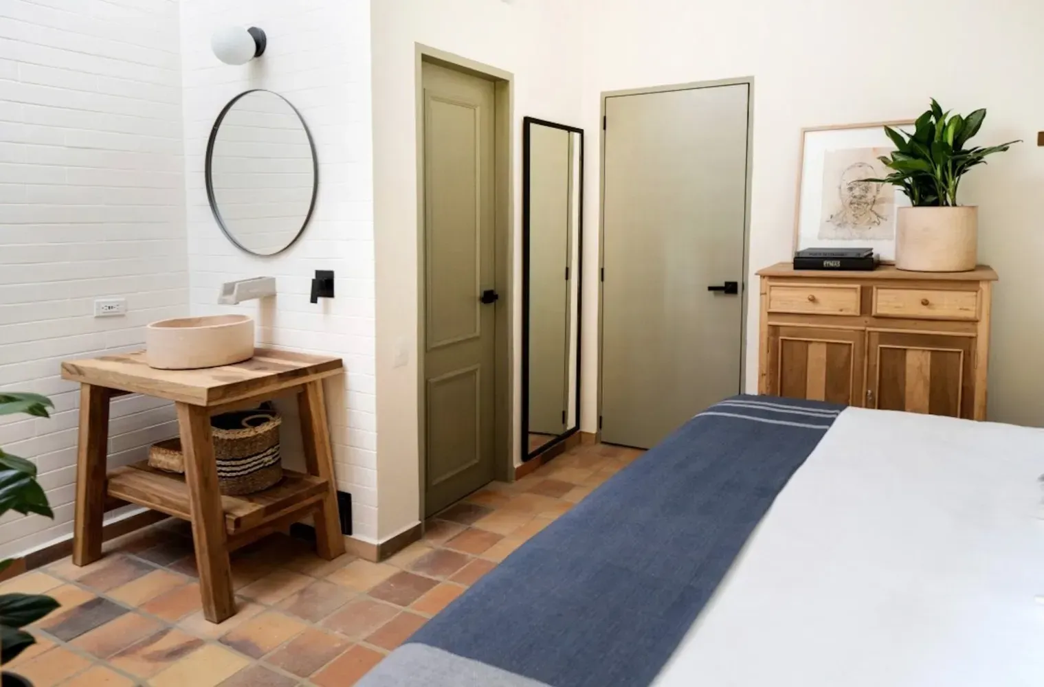 A bedroom with a bed , dresser , sink and mirror.