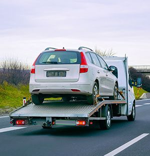 A white car being towed on a flatbed tow truck on a highway.