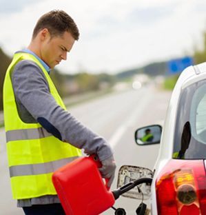 Man in yellow vest pouring gas into a car on a road.