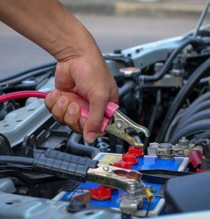 Hand attaching jumper cable to a car battery; close-up on engine.