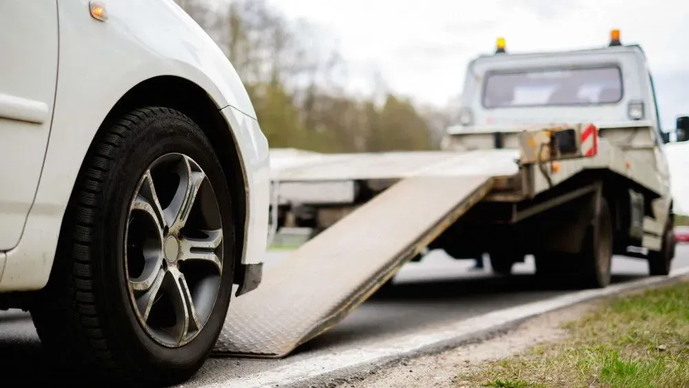 White car being loaded onto a tow truck's ramp on a roadside.