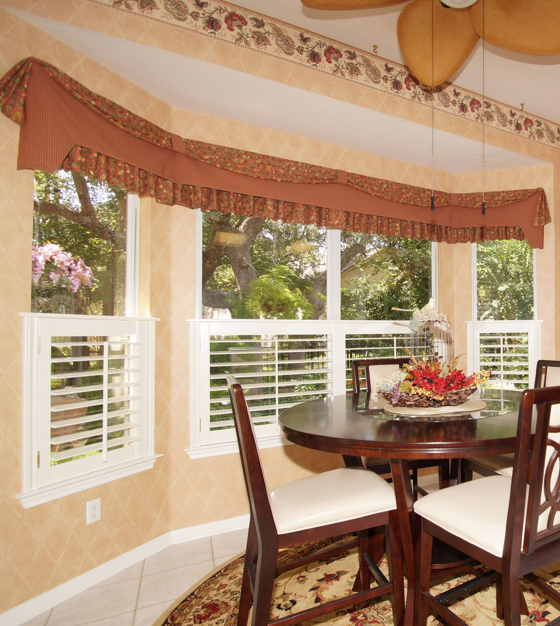 Dining room with a bay window, dark wooden table, white chairs, and a brown valance.