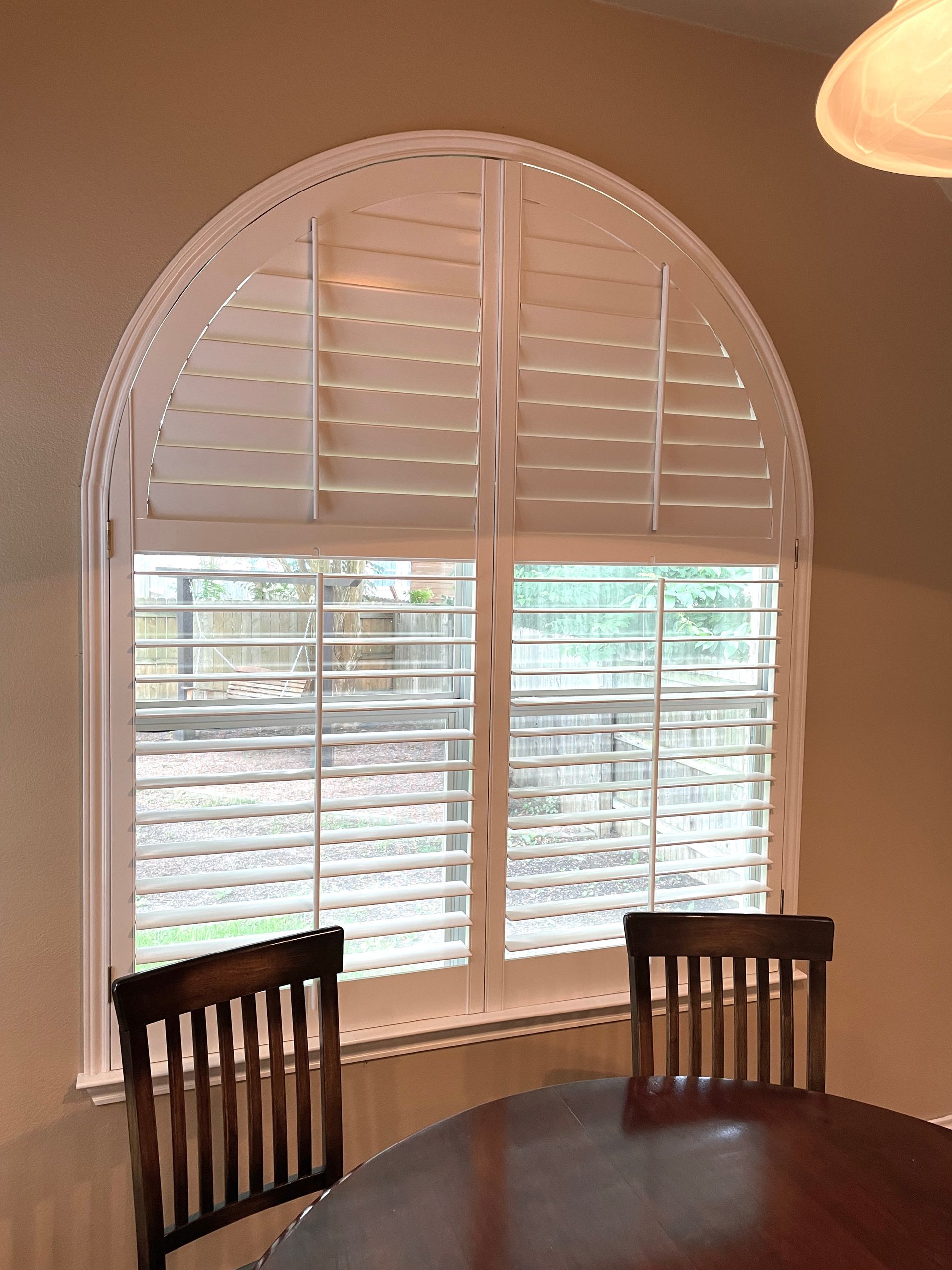 A table and chairs in front of a window with arched shutters