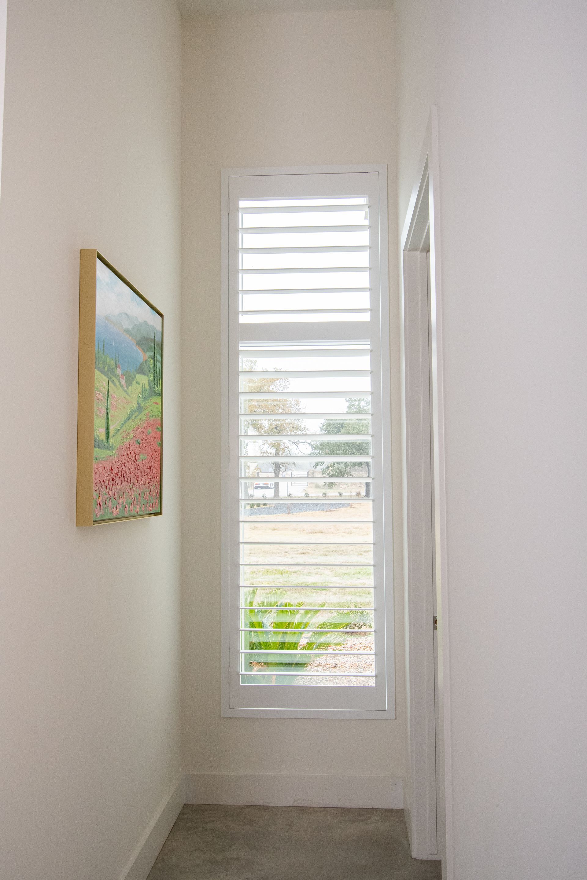A hallway with a large window and a painting on the wall.