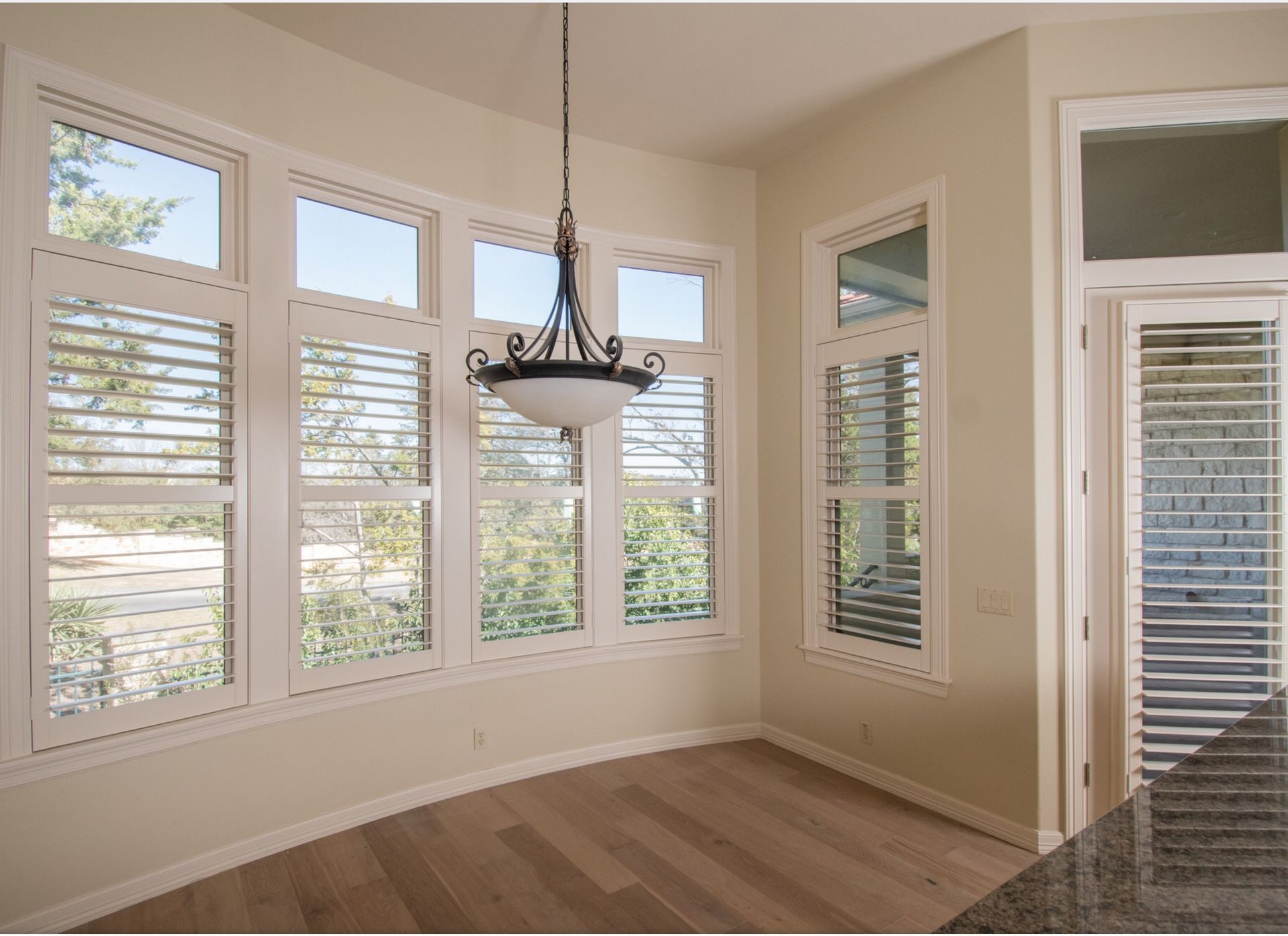 Dining area with shuttered windows, chandelier, light wood floors, and neutral walls.
