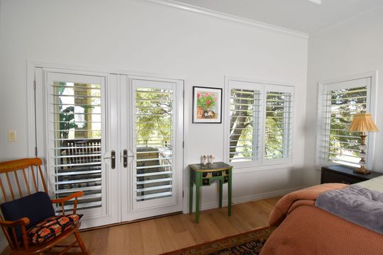 bedroom with white louvered shutters in the open position, showcasing views to the outside