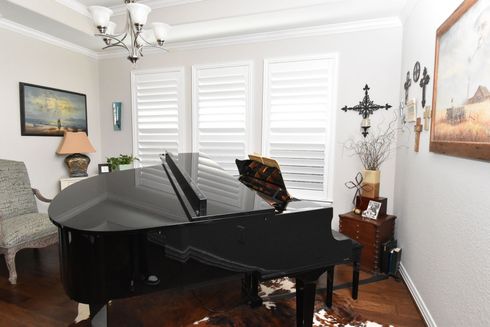 Open white plantation shutters with light streaming in piano room 
