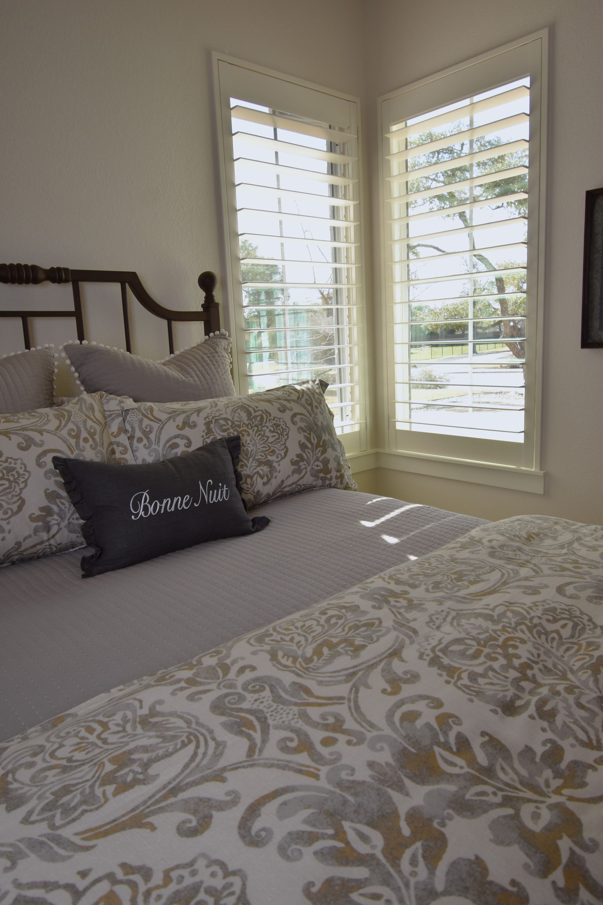 A bedroom with a bed , pillows , and a window with shutters.