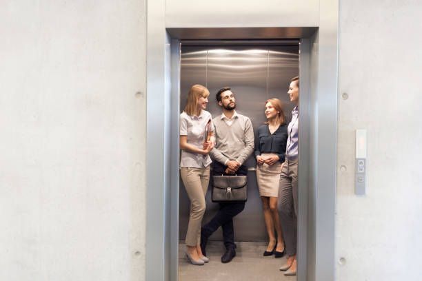 A group of people are standing in an elevator talking to each other.