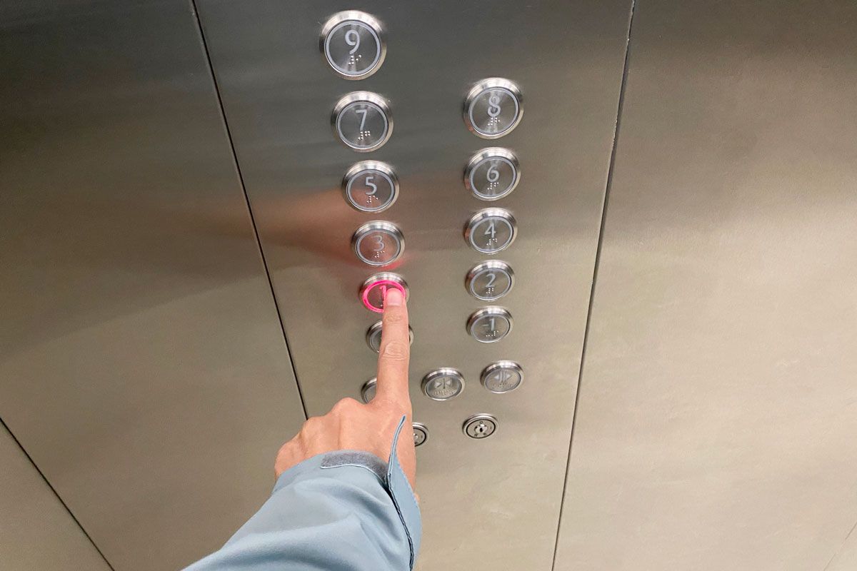 A person is pressing a red button in an elevator.
