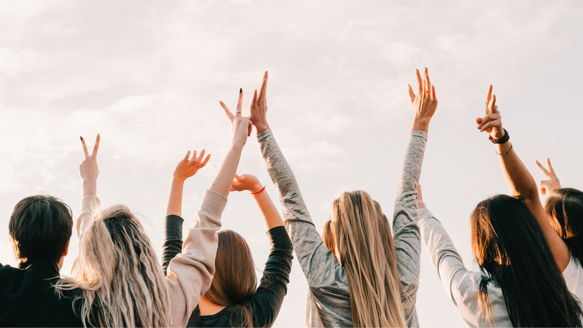 People with arms raised towards a bright sky, some showing peace signs and victory gestures.
