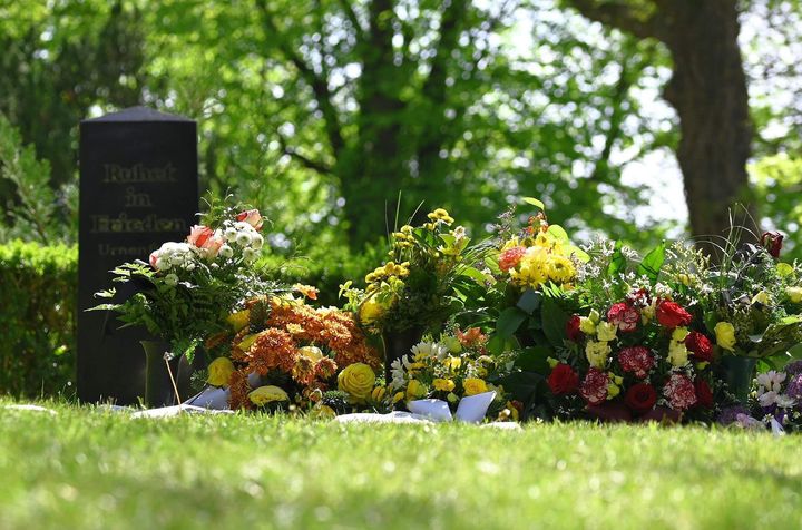 A grave in a cemetery with flowers in front of it.
