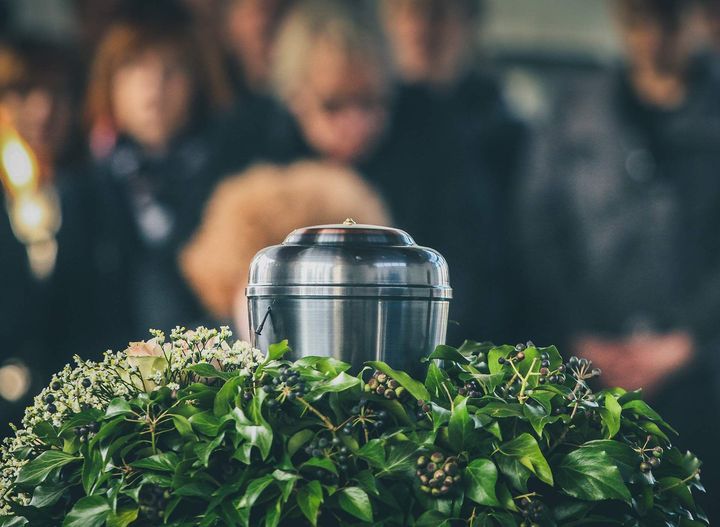 A silver urn is sitting on top of a wreath of flowers at a funeral.