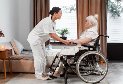 A nurse is standing next to an elderly woman in a wheelchair.