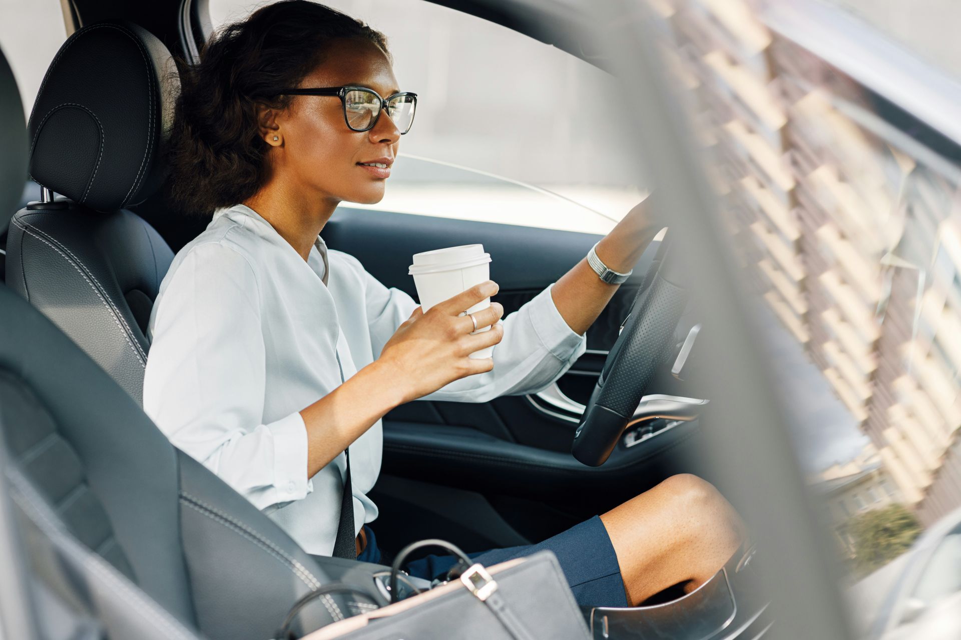 A woman is sitting in the driver 's seat of a car holding a cup of coffee.