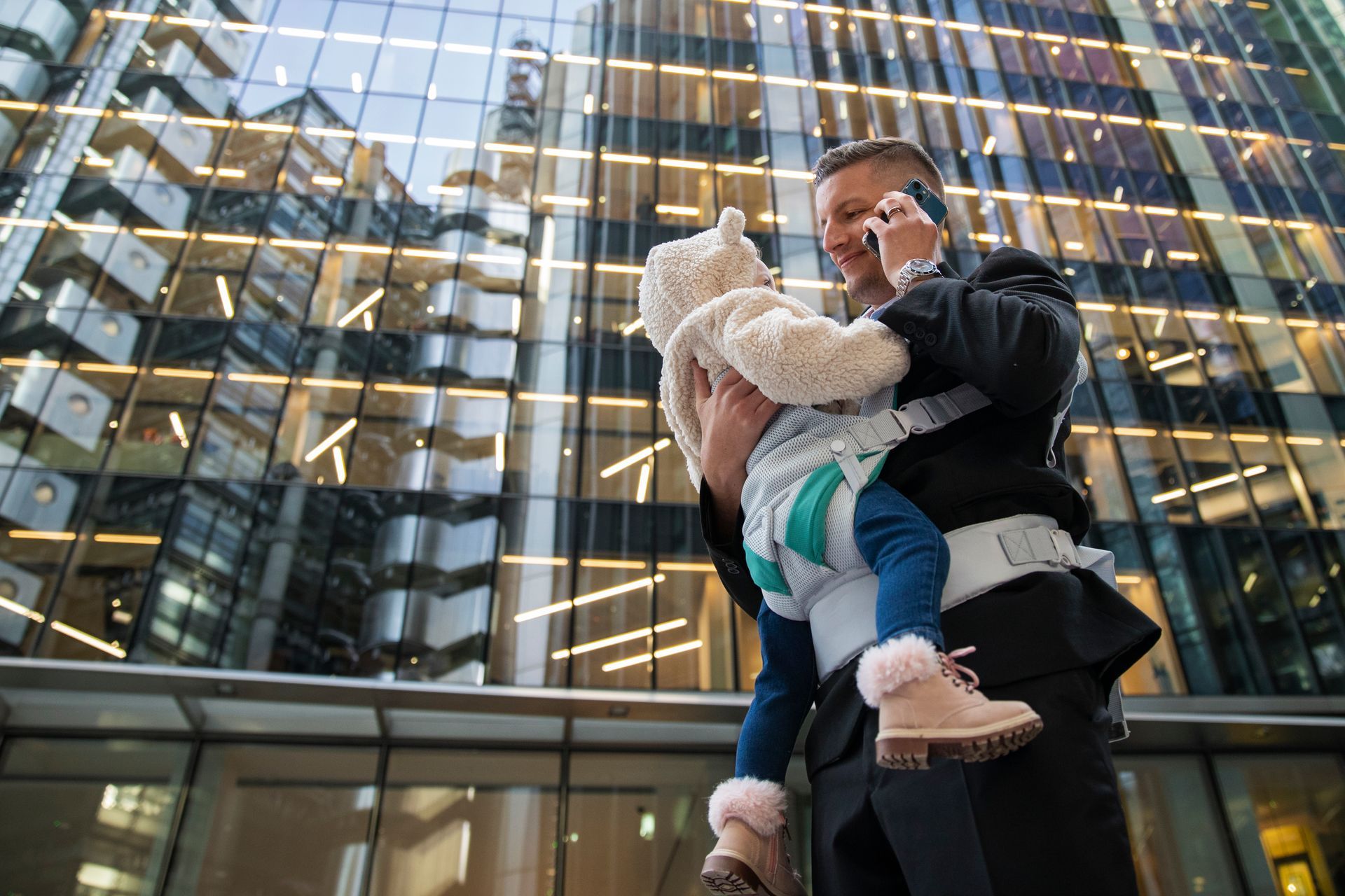 A man is holding a baby in a carrier while talking on a cell phone.