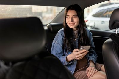 A woman is sitting in the back seat of a car holding a cell phone.