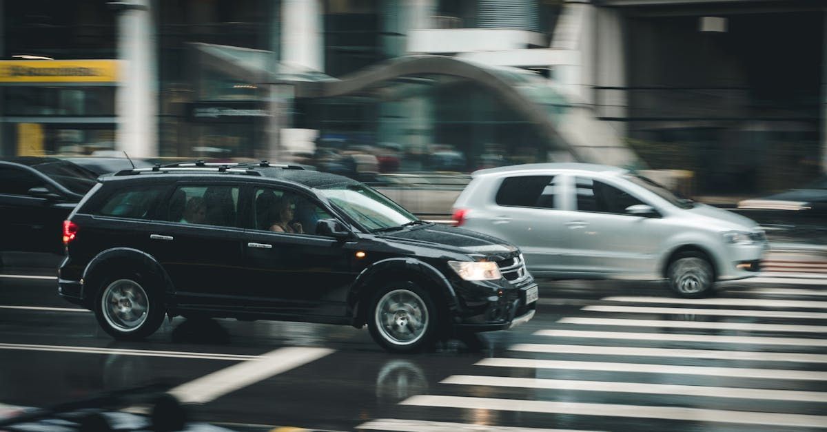 A black suv and a white suv are driving down a wet city street.