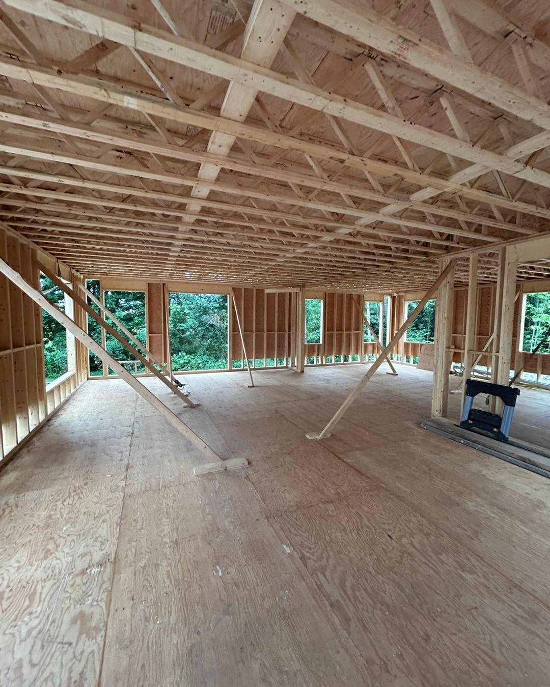 Charpente en bois d'un bâtiment en construction, avec fenêtres ouvertes et supports visibles.