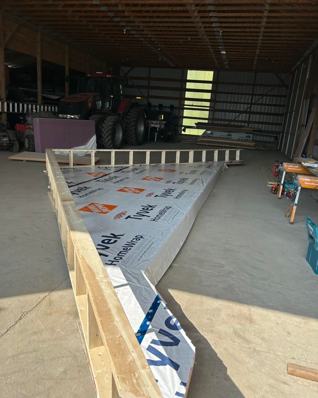 Charpente en bois isolée à l'intérieur de la grange ; tracteur en arrière-plan.