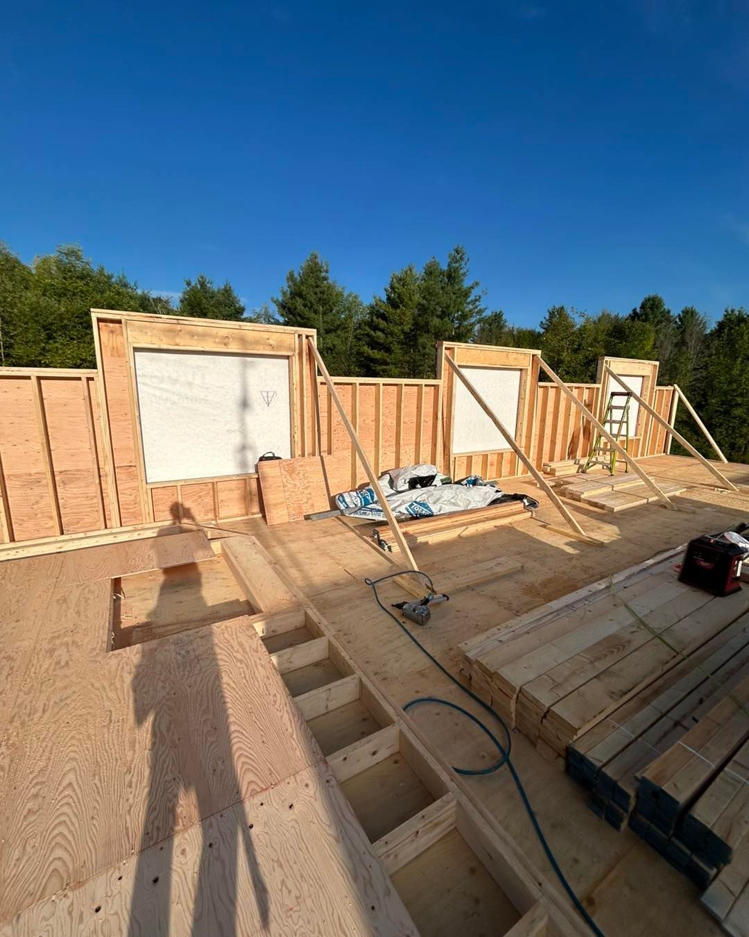 Chantier de construction, charpente en bois inachevée d'un bâtiment sous un ciel bleu dégagé.