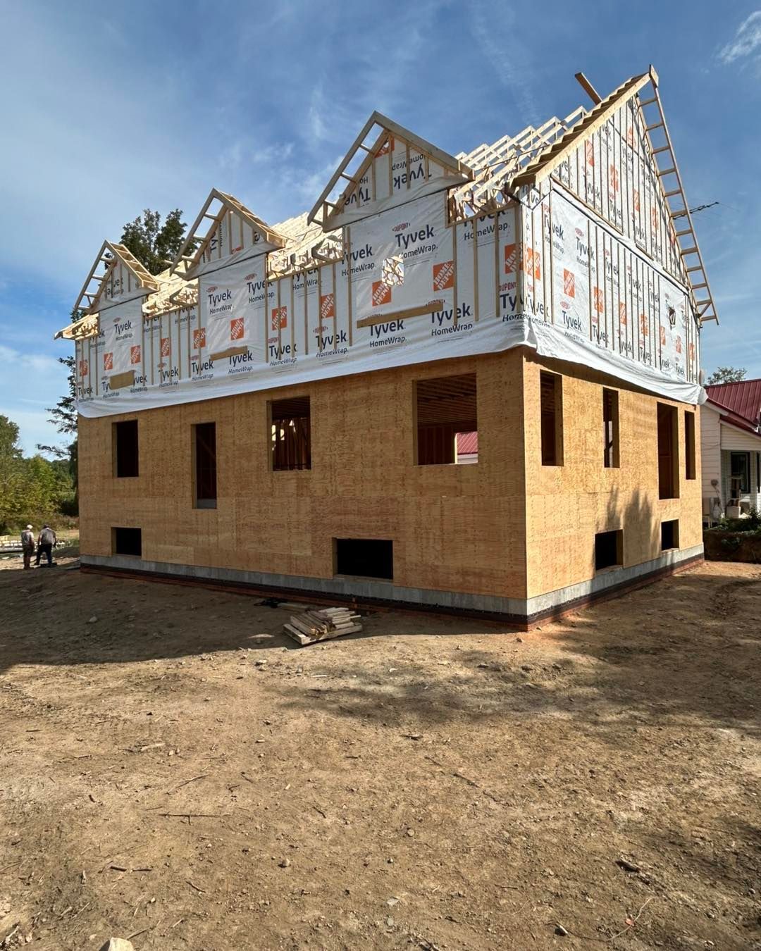 Maison à deux étages en construction, avec bardage en bois et charpente de toit apparente.
