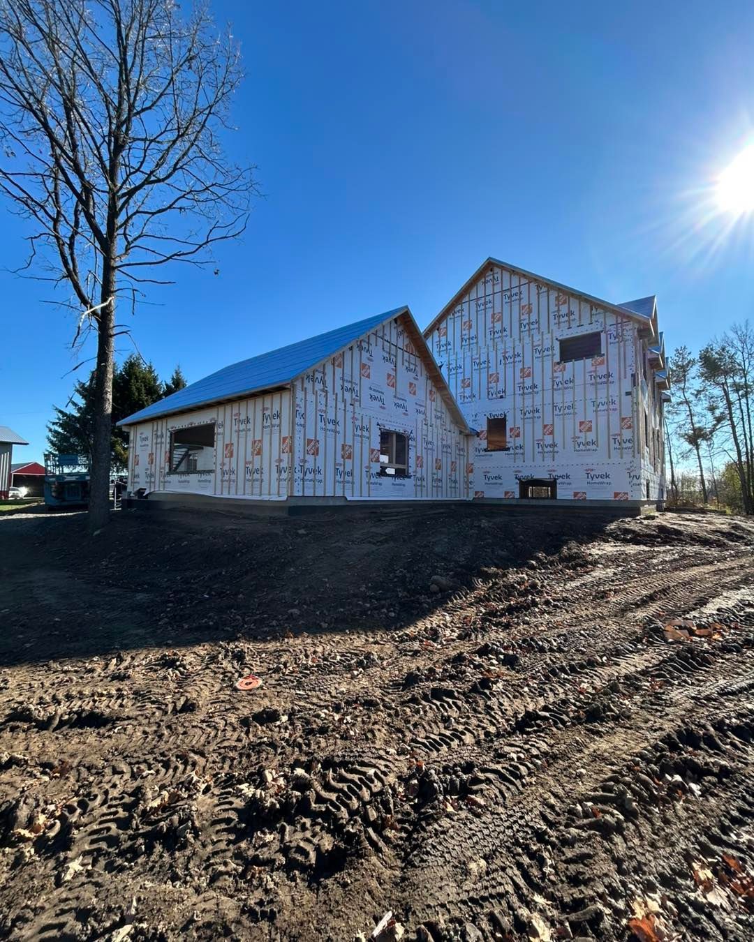 Une maison neuve en construction par une journée ensoleillée. La structure est recouverte d'isolant blanc.