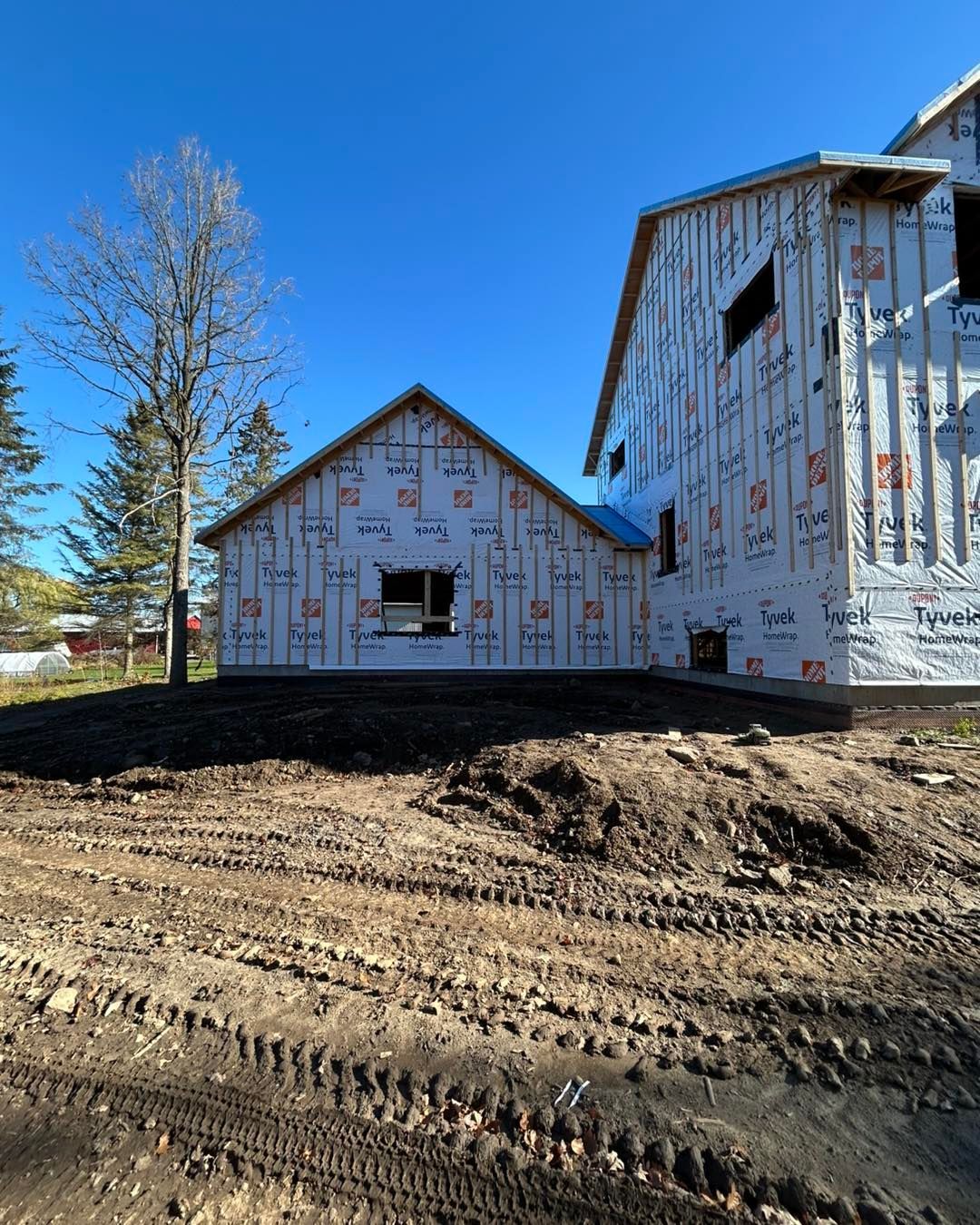 Chantier de construction, bâtiment inachevé recouvert de Tyvek, ciel bleu clair.
