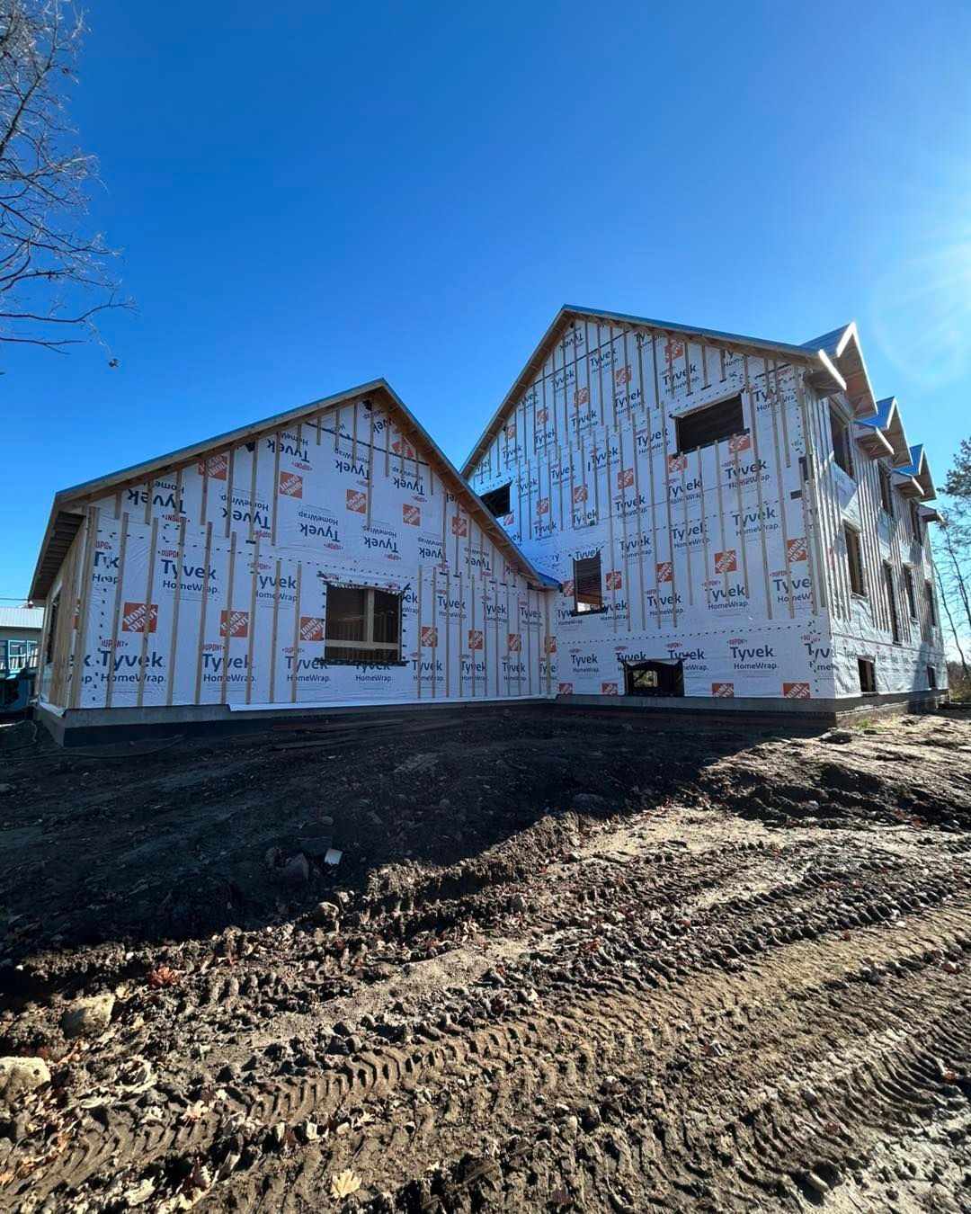 Des bâtiments en construction, enveloppés de Tyvek, se détachent sur un ciel bleu azur, sur un terrain nivelé.