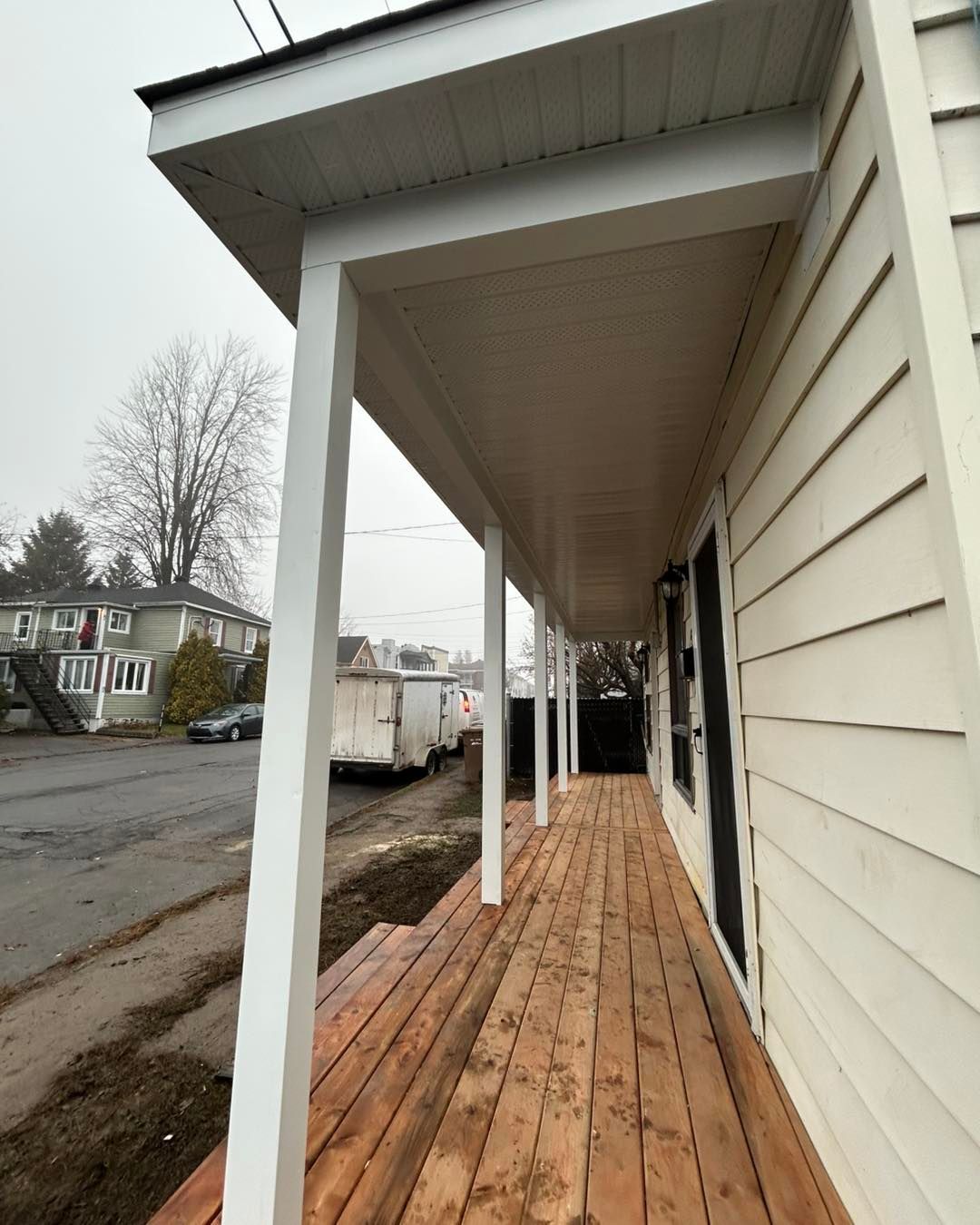 Porche peint en blanc avec plancher en bois. Des colonnes soutiennent un plafond blanc. Vue sur la rue.