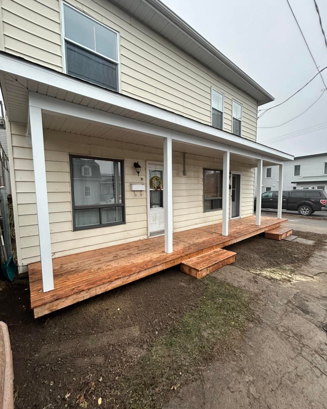 Maison beige à deux étages avec porche et marches en bois neufs ; vue extérieure.