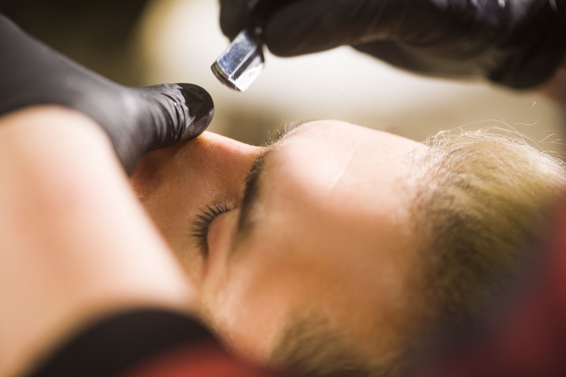 Barber giving a client a haircut in a shop. Client's eyes are closed, barber's hands are focused on the haircut.