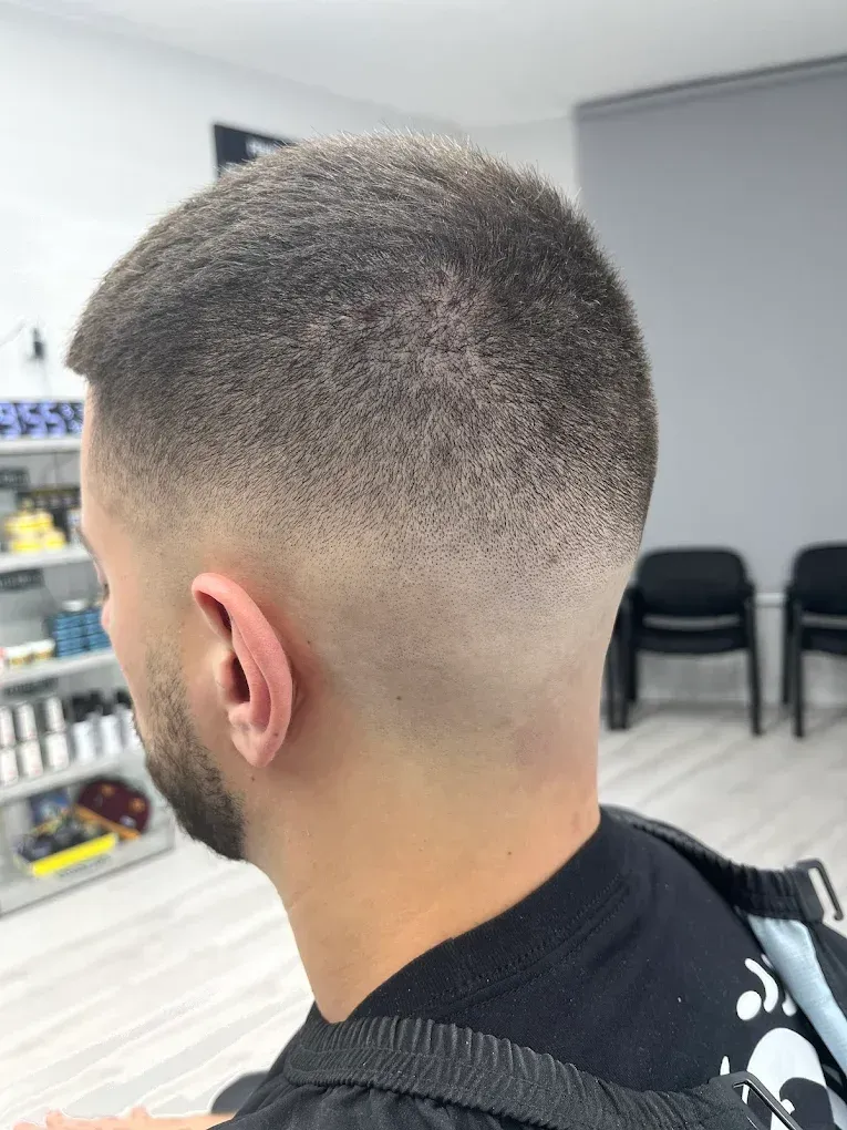 Man getting a haircut in a barbershop; barber adjusting hair, holding scissors, interior.
