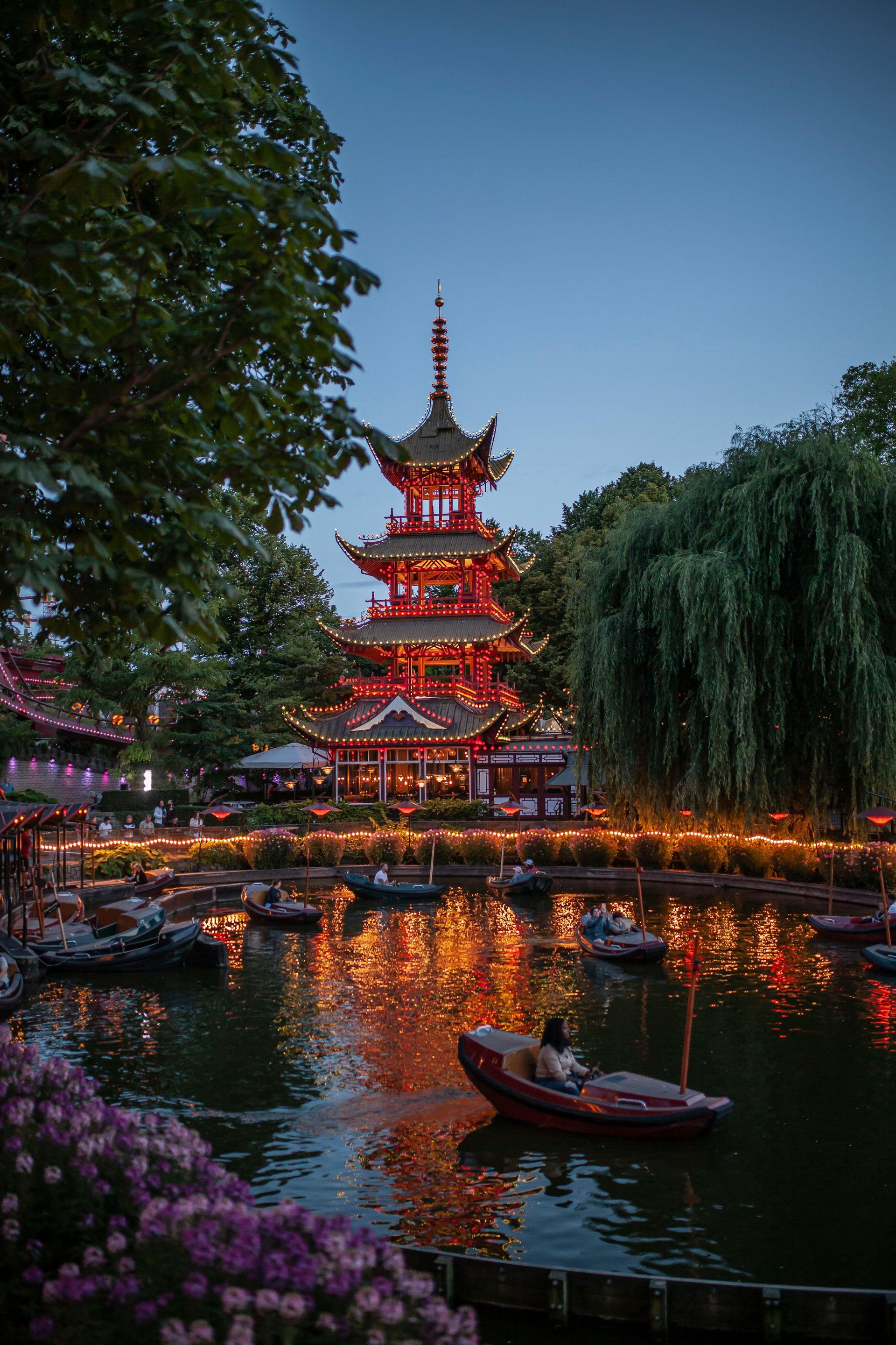 A man is in a boat in front of a pagoda in a park.