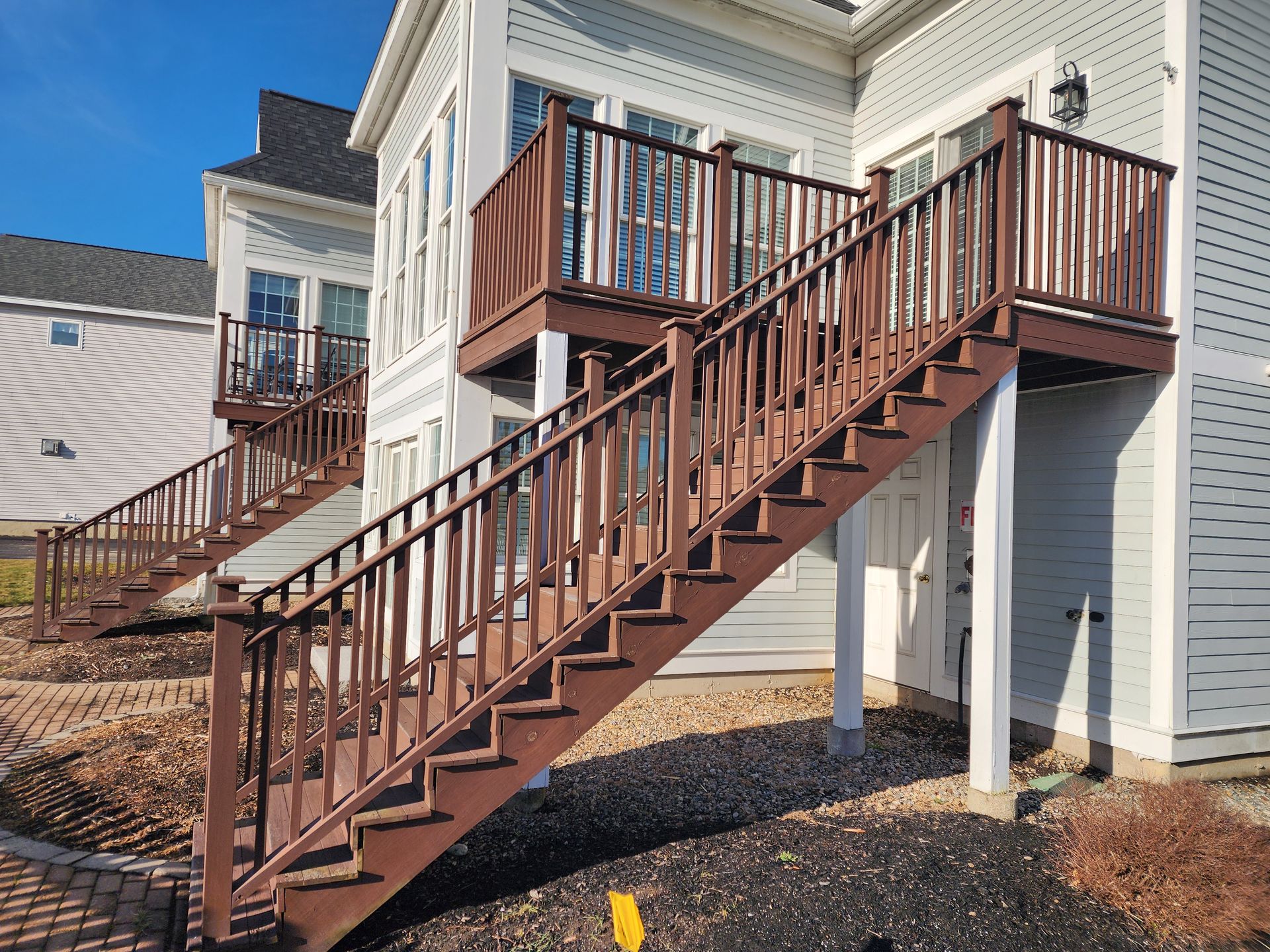 Brown wooden staircase leading up to a light blue building with a deck.