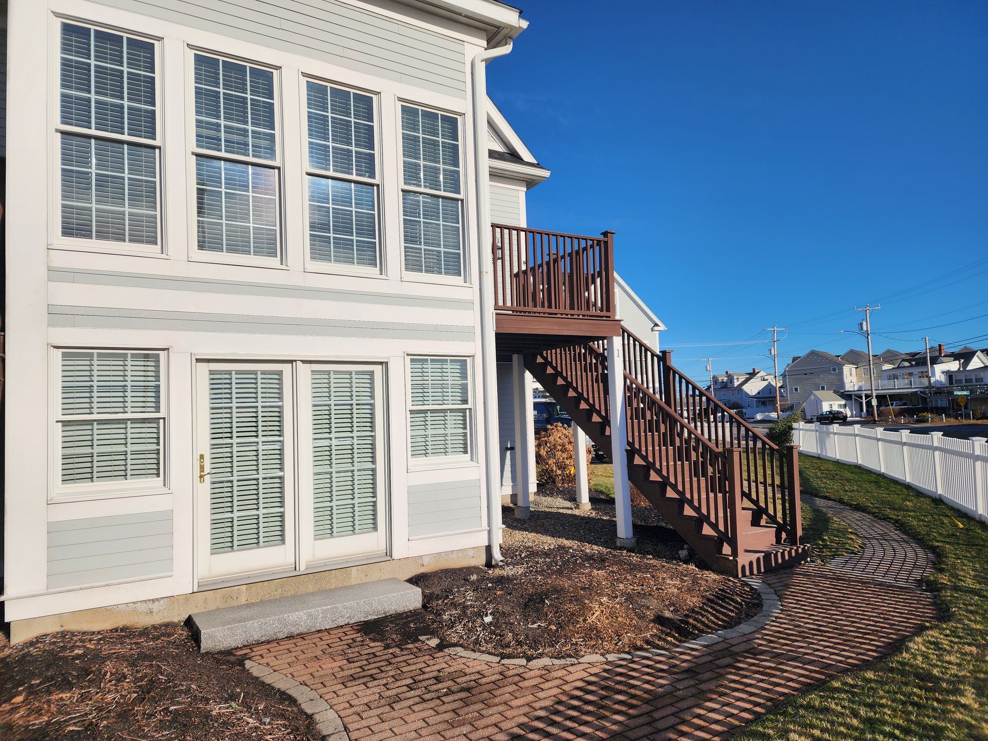 House exterior with brown wooden deck stairs, large windows, and a blue sky.