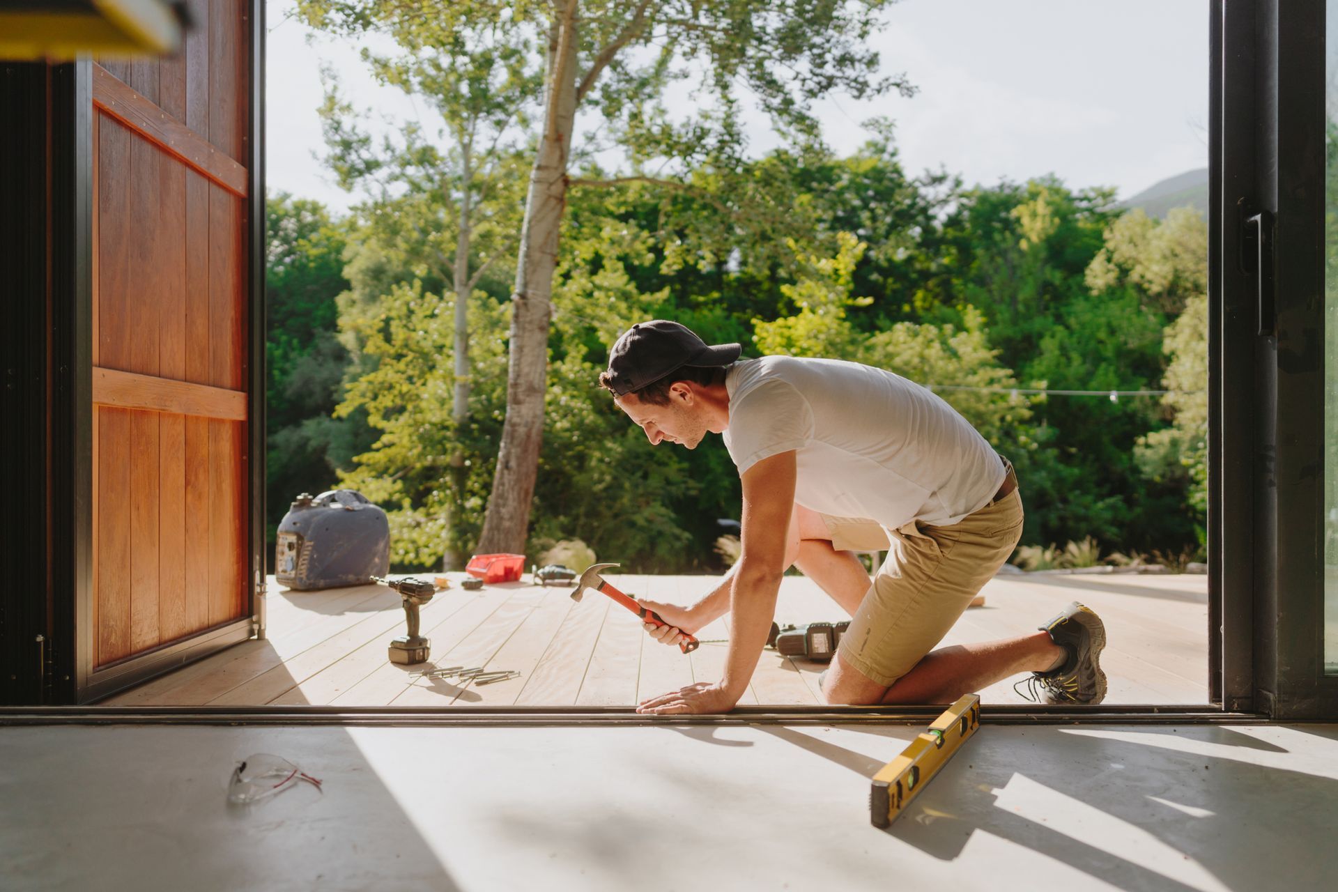 Deck installation in progress with worker kneeling, tools, and lush green background.