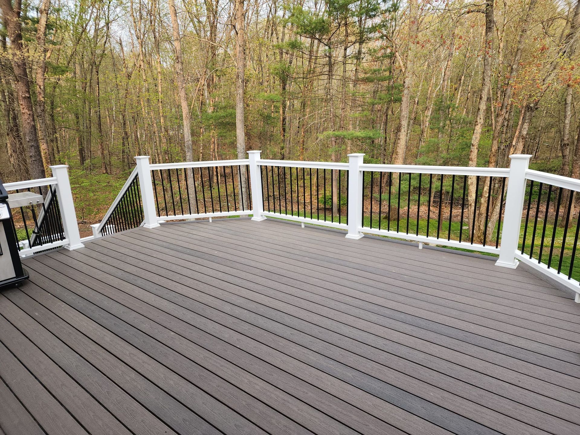 A wooden deck with a white railing and trees in the background - Plaistow, NH - Dynamic Deck Solutions